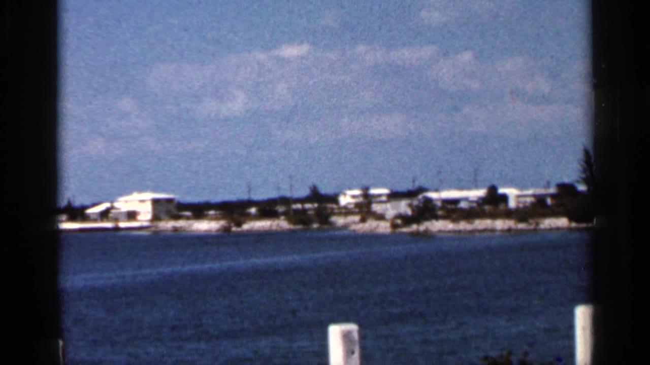 Wide water view toward a sandy shoreline with low white buildings under a blue sky.