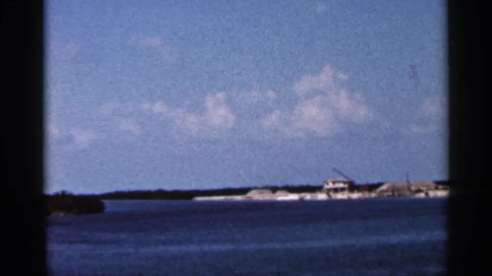 Soft 8mm view of a Florida shoreline, with calm water, a small distant building, and apparent construction equipment on the horizon.