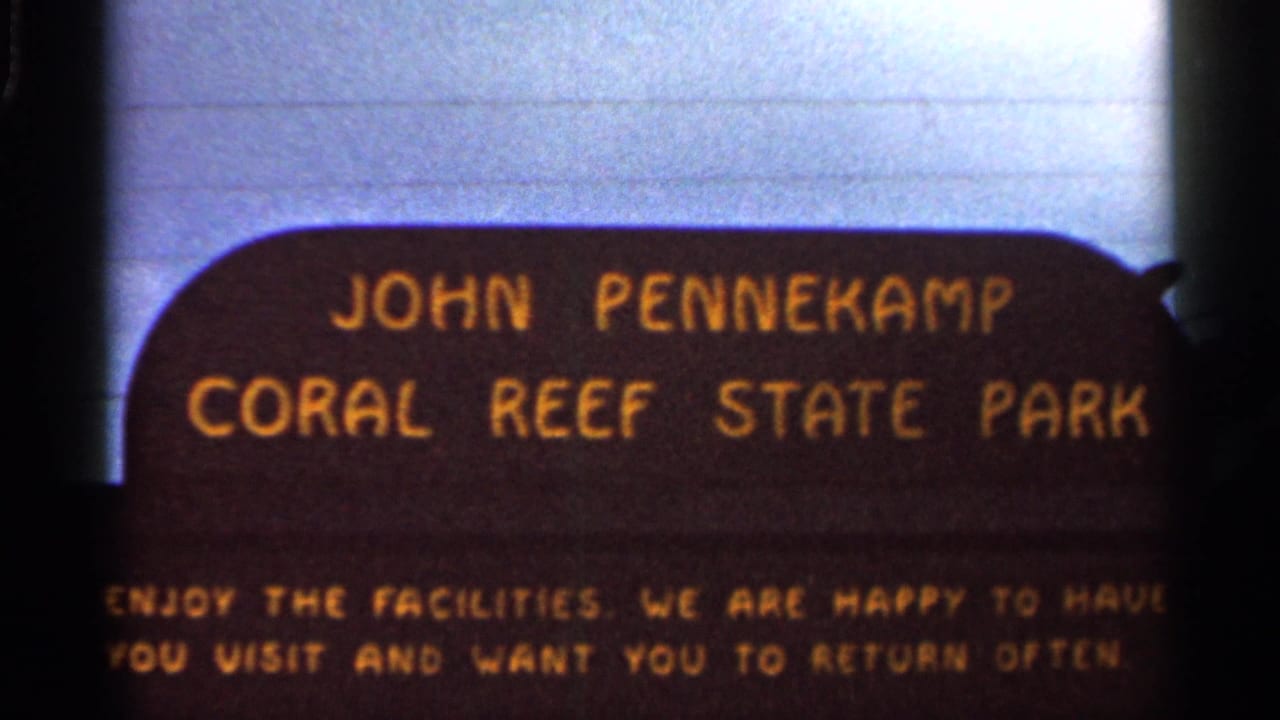 Dark brown John Pennekamp Coral Reef State Park sign with yellow lettering against a pale sky.