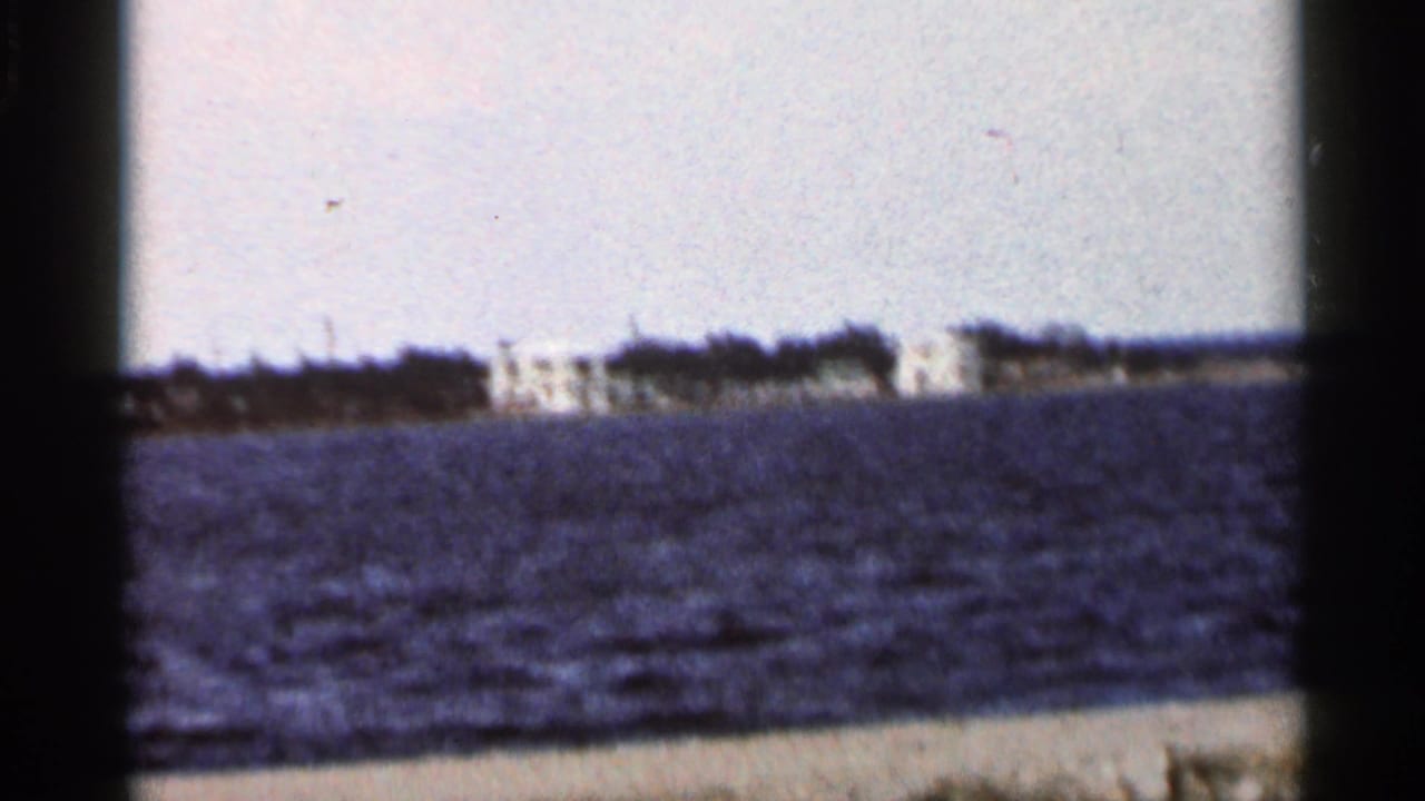 Distant white buildings across rippled water beneath a pale sky.