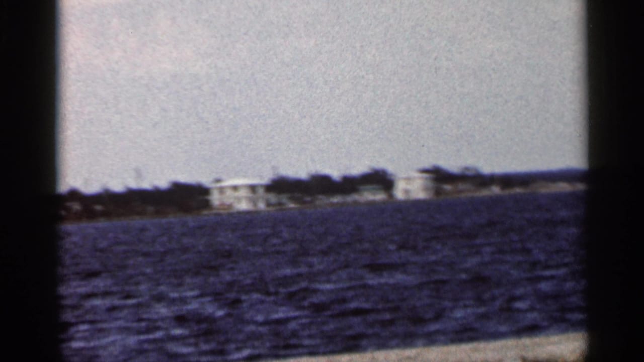 Low shoreline with white buildings seen across dark blue water.