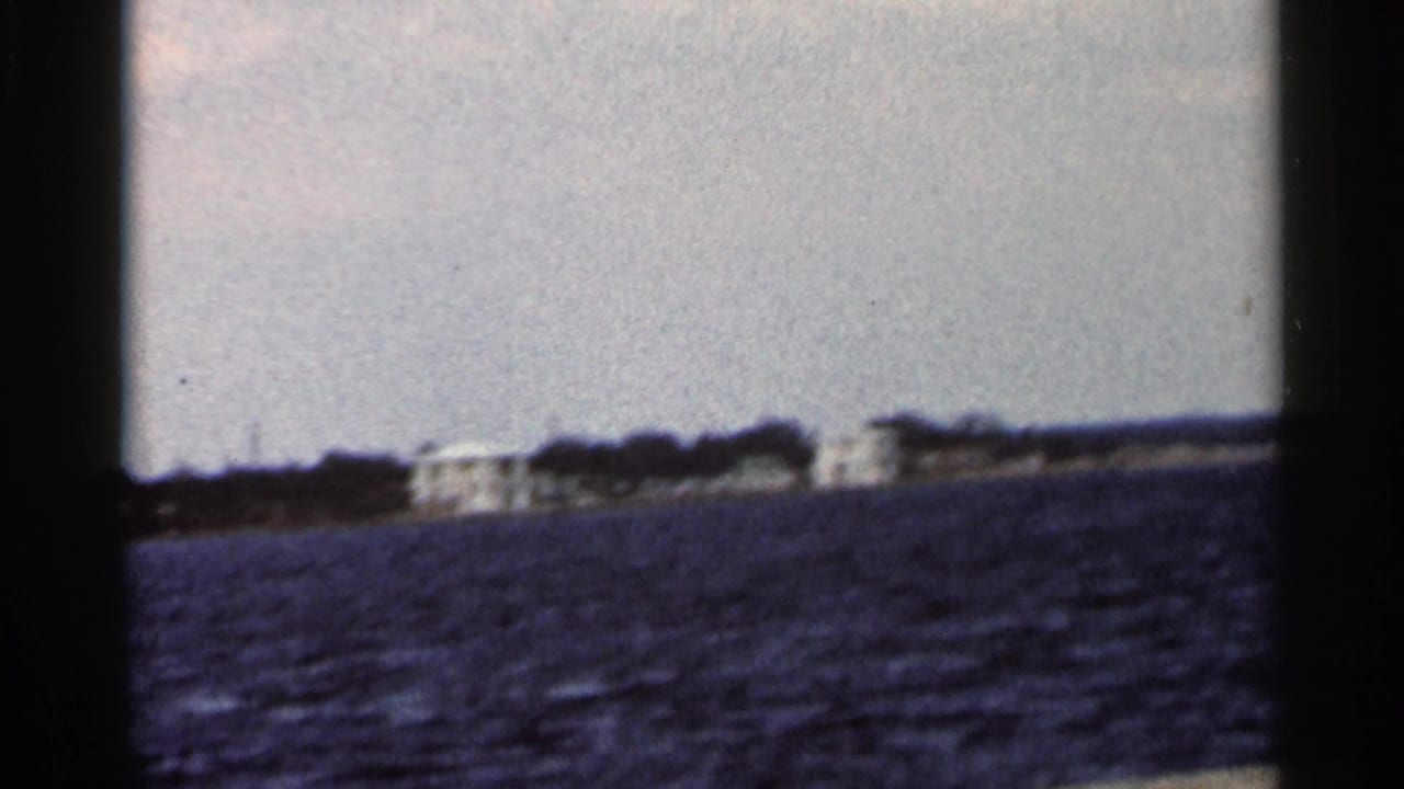 1966 Florida coastal view showing distant white structures, a dark treeline, and rippled water from a home-movie vantage point.