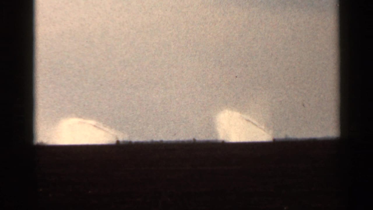 1966 Florida 8mm frame with pale sprinkler-like or spray forms near the horizon against a bright, grainy sky.