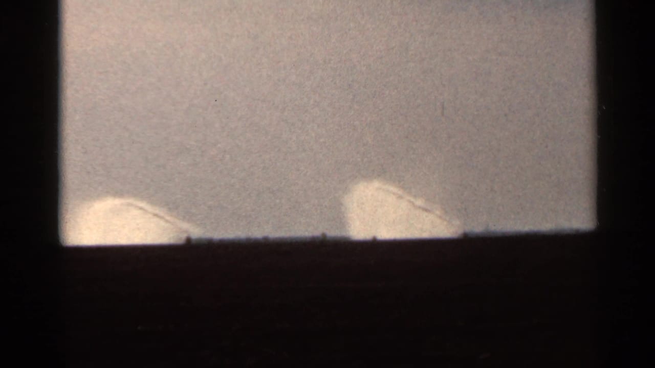 1966 Florida 8mm frame showing two pale curved spray or sprinkler forms against a bright sky and dark horizon.