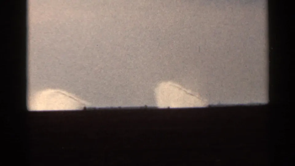 1966 Florida 8mm frame showing two pale curved spray or sprinkler forms against a bright sky and dark horizon.