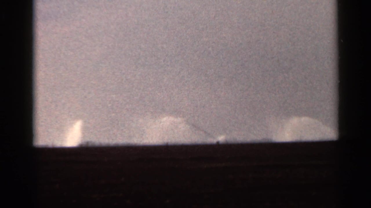 1966 Florida 8mm frame showing faint irrigation spray along a low horizon under a pale sky.