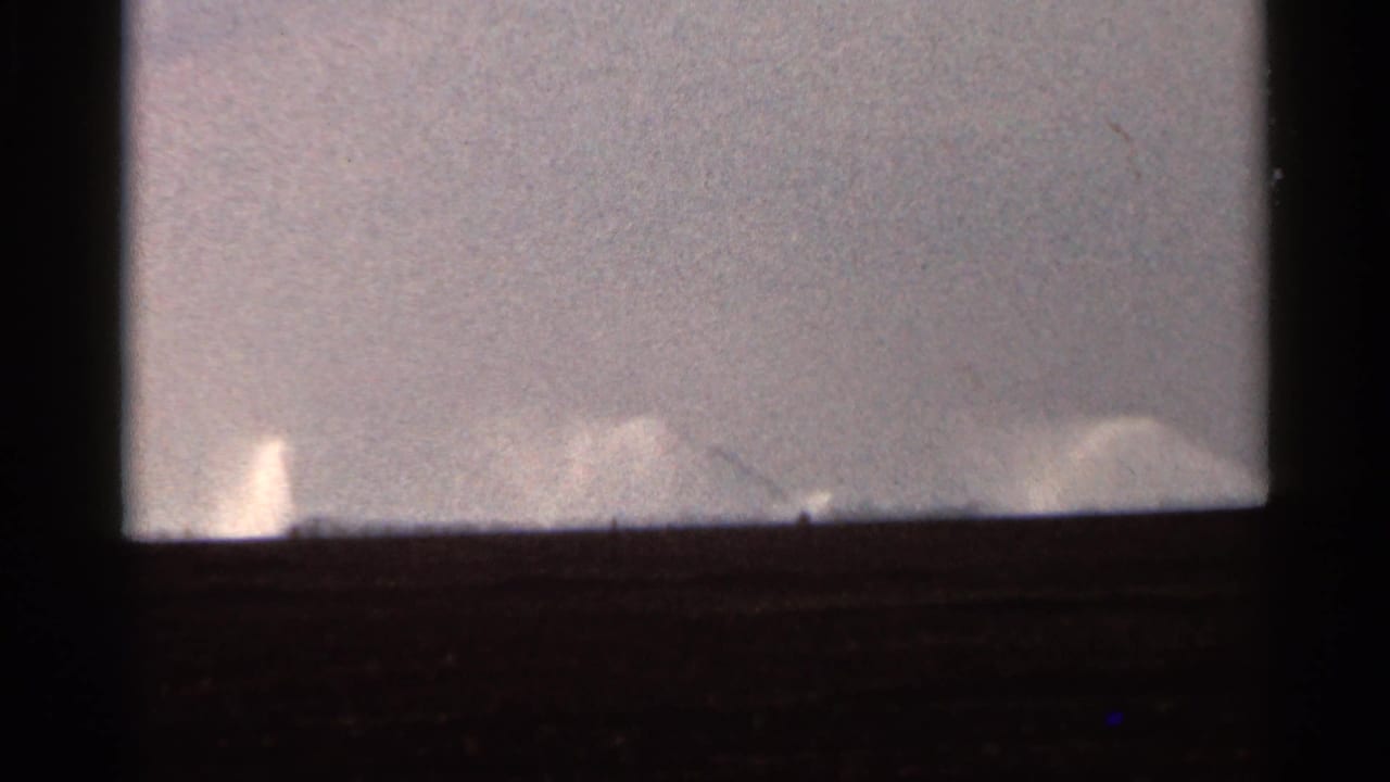 1966 Florida 8mm view of low, distant irrigation spray with dark frame edges and muted exposure.