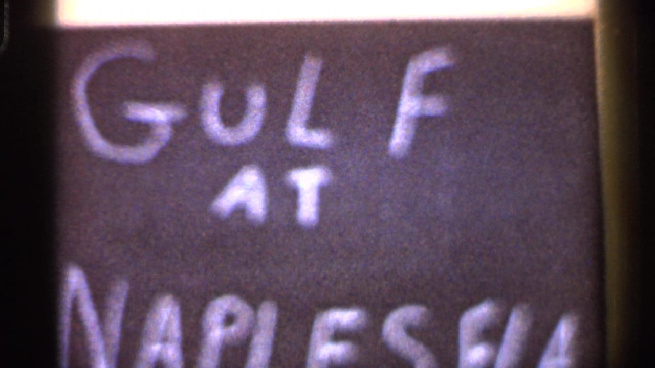 Hand-painted sign with white lettering reading "GOLF AT" above partial Naples, Florida text.