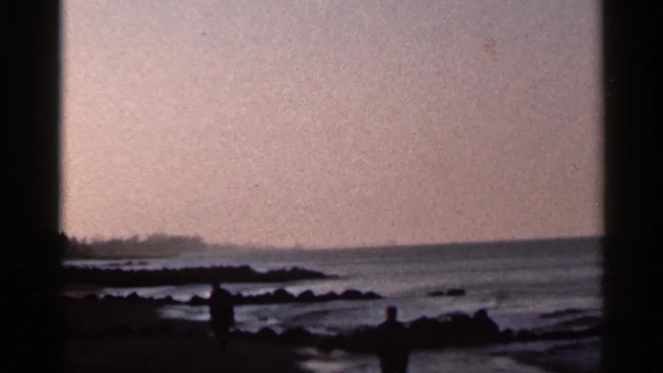 1966 Florida beach scene with distant silhouetted figures near rocks, wet sand, and a calm ocean horizon.