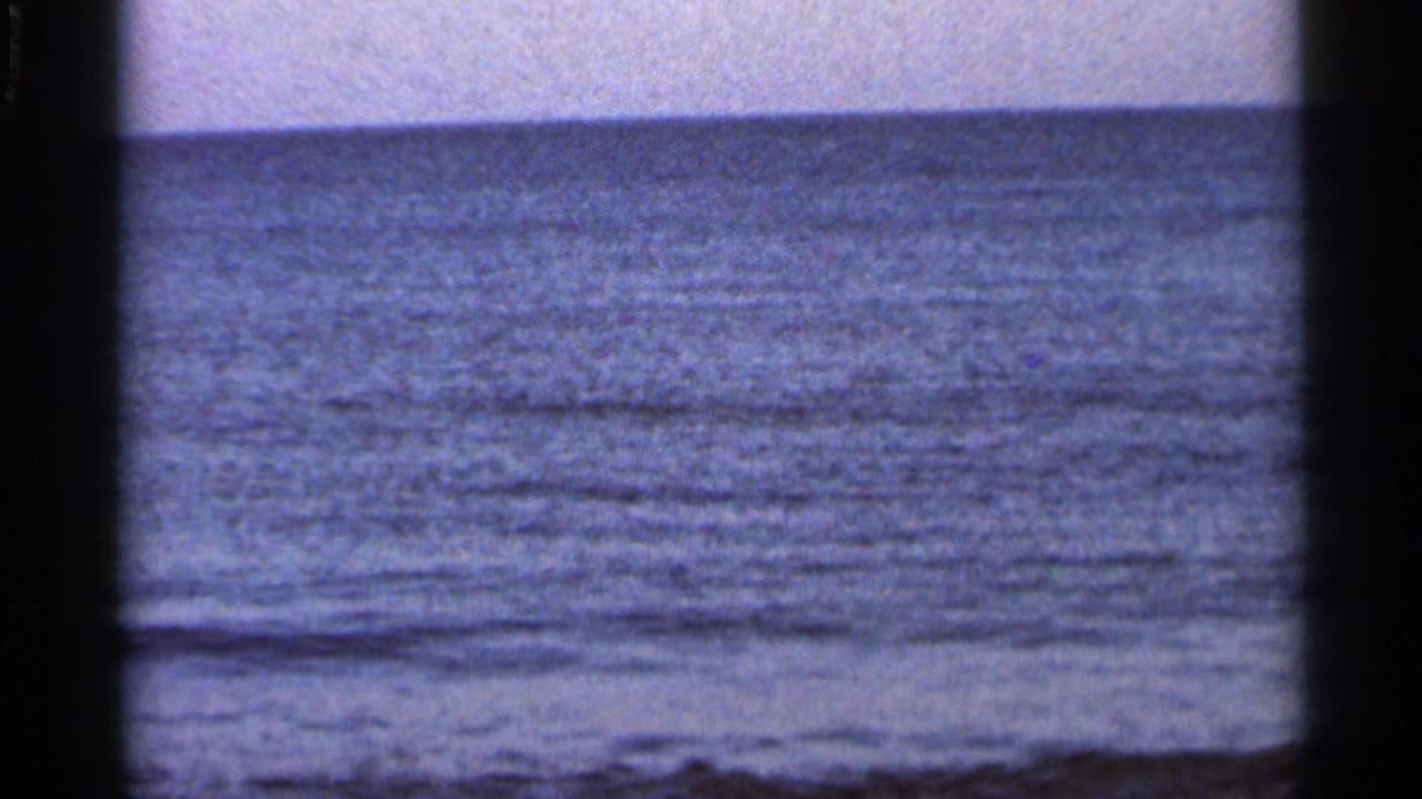 1966 Florida 8mm frame showing textured blue water, a low horizon, hazy sky, and visible film grain.