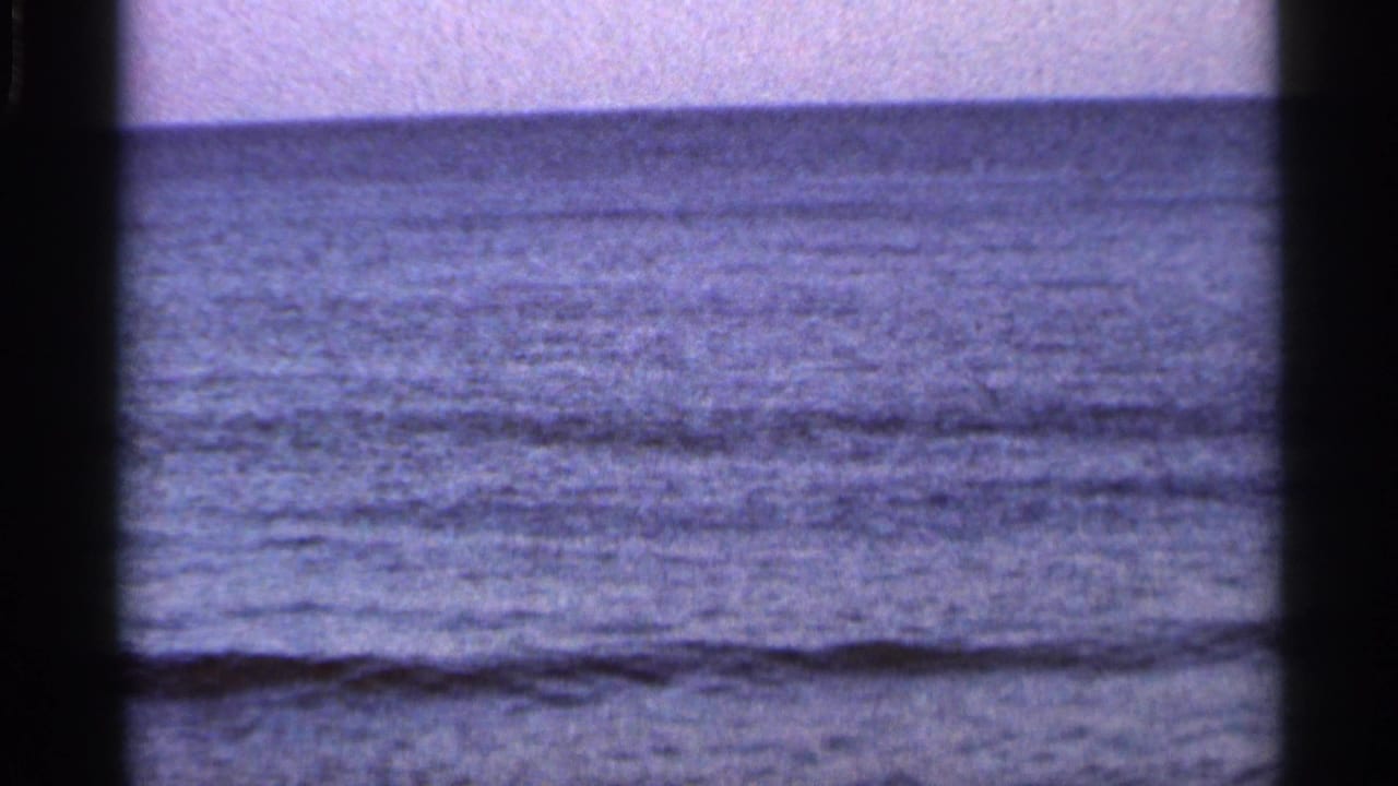 1966 Florida coastal frame with low waves, flat ocean horizon, pale sky, and dark 8mm gate borders.
