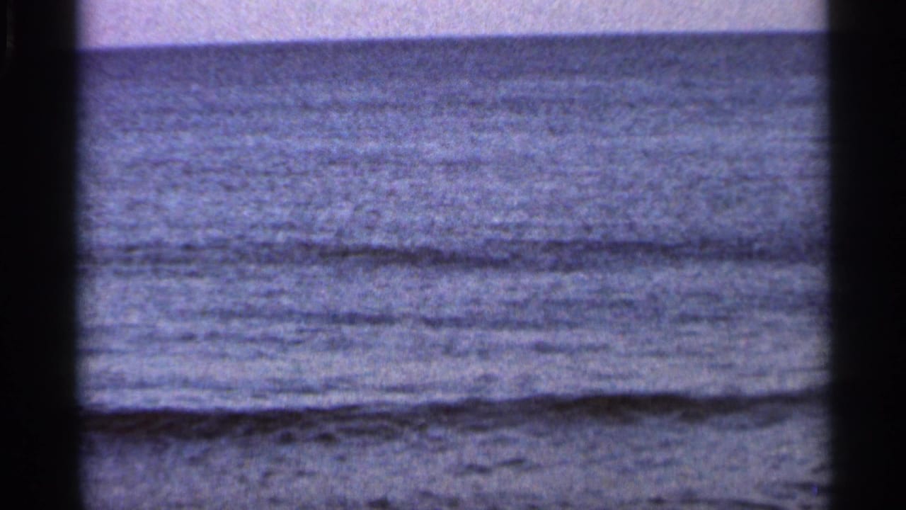 1966 Florida 8mm frame showing a calm ocean horizon, low surf, muted color, and dark projector-frame edges.