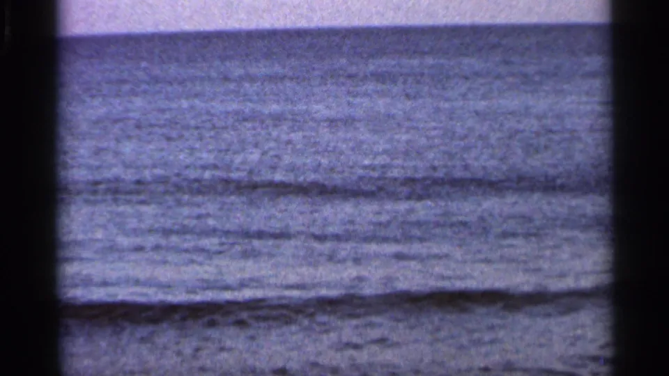 1966 Florida 8mm frame showing a calm ocean horizon, low surf, muted color, and dark projector-frame edges.