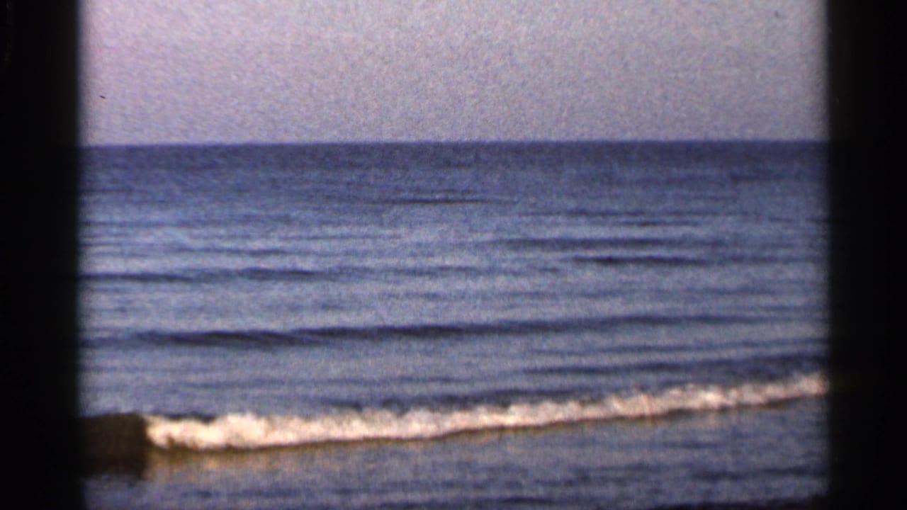 1966 Florida 8mm view of gentle surf washing onto a sandy beach, with ocean horizon and muted film color.