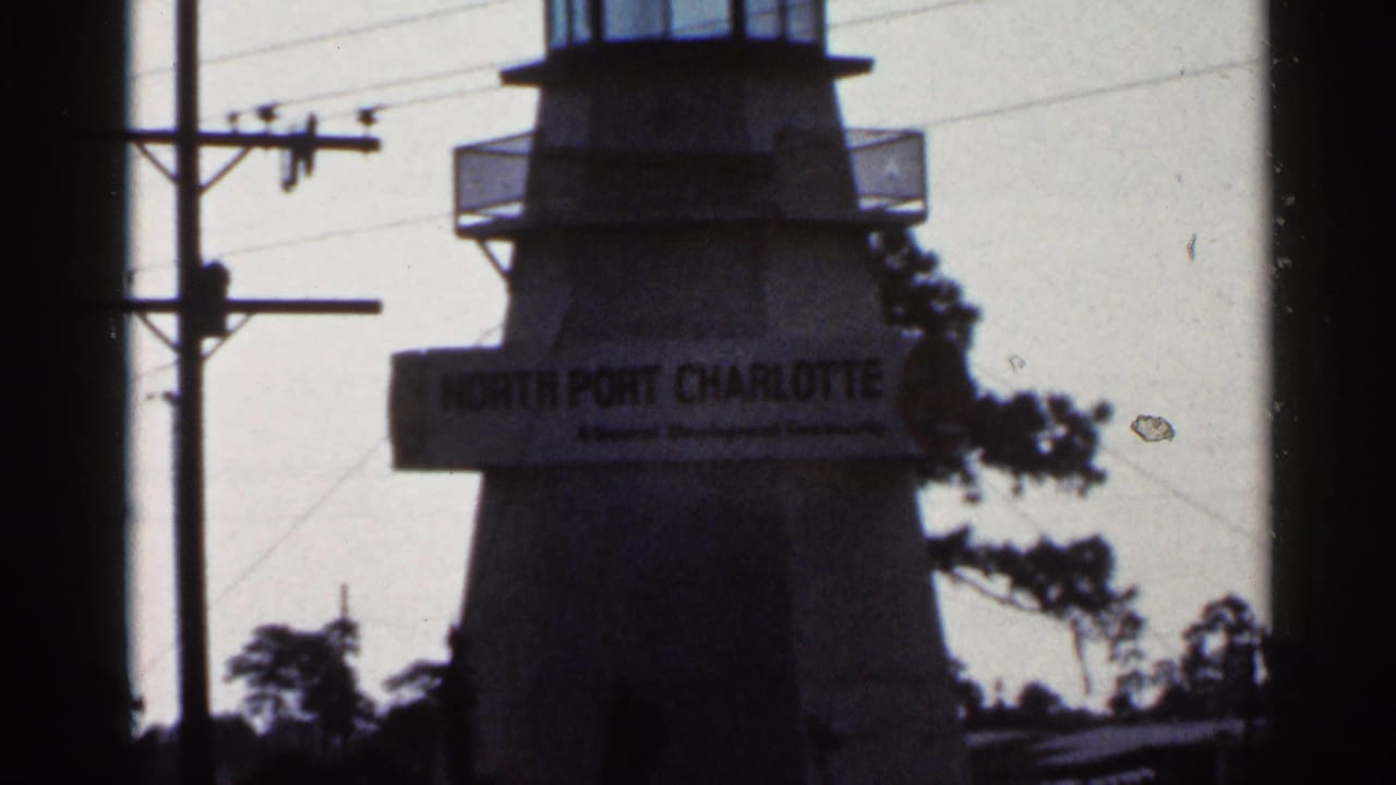 Tower with North Port Charlotte sign, power lines, trees, and dark window-frame edges.