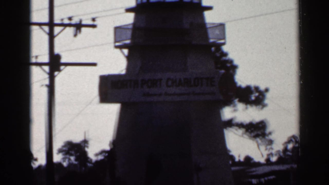 1966 Florida home-movie frame with a soft, dark view of the North Port Charlotte tower sign beside utility lines and trees.
