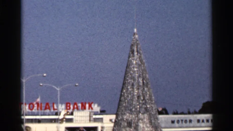 Tall public Christmas tree with star topper in front of partial National Bank and Motor Bank signage in Florida.