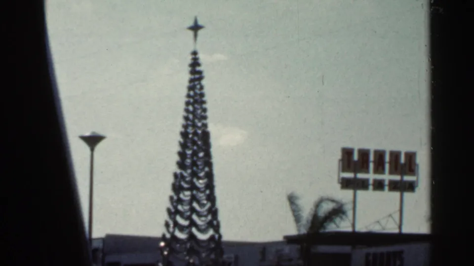 1966 Tampa Bay-area frame with an outdoor Christmas tree, star topper, palm trees, and visible roadside signage.