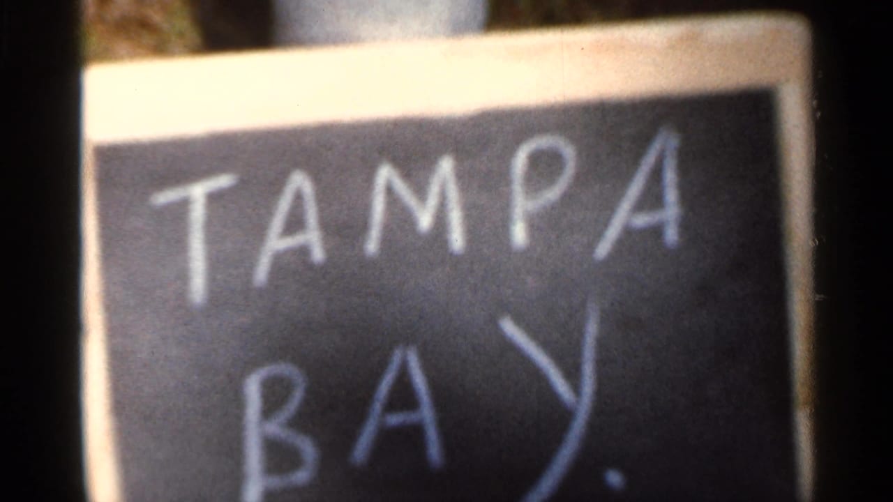Close 8mm frame of a handwritten chalkboard title card reading TAMPA BAY, used as a location marker.