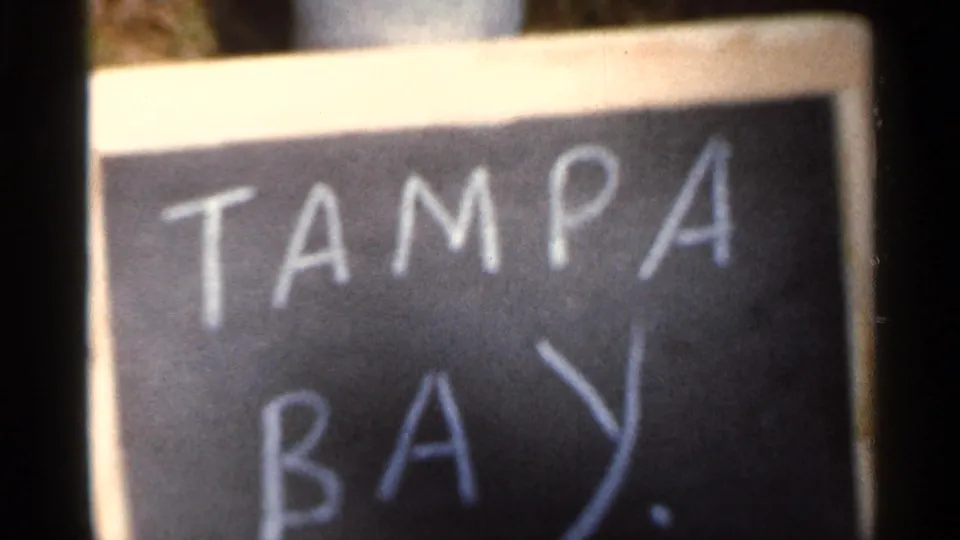 Close 8mm frame of a handwritten chalkboard title card reading TAMPA BAY, used as a location marker.