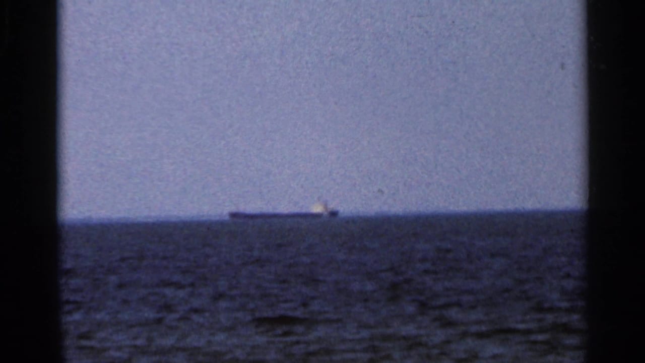 1966 Florida 8mm frame showing a distant ship low on the ocean horizon, seen through dark film gate borders.