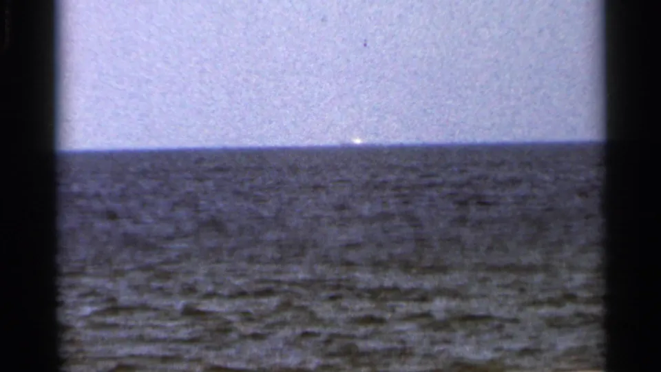 1966 Florida 8mm frame showing textured water, pale sky, and a faint bright object near the distant horizon.