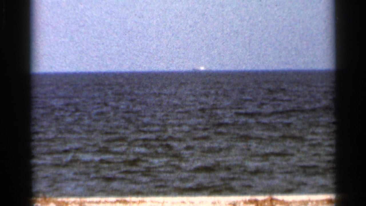 1966 Florida 8mm frame showing the sea horizon and a distant bright bridge-like or vessel shape across the water.