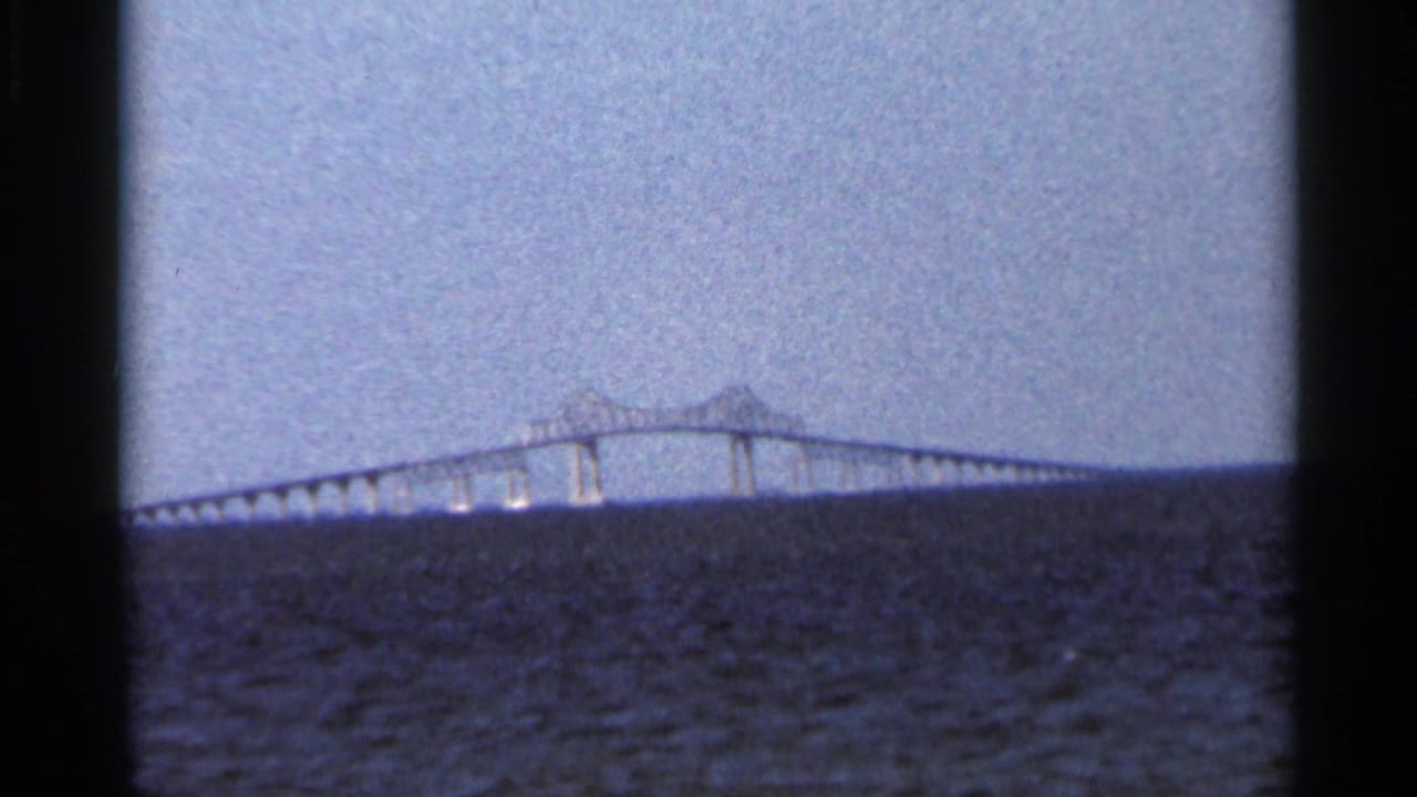 Distant bridge crossing open water under a hazy sky, framed by dark film borders.