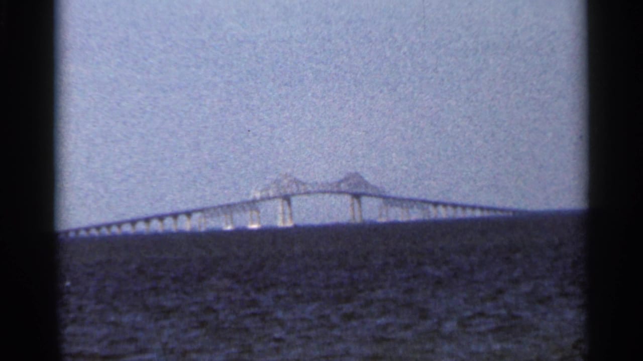 Distant Florida bridge across open water in a 1966 home-movie frame, with visible piers, soft focus, and dark frame borders.