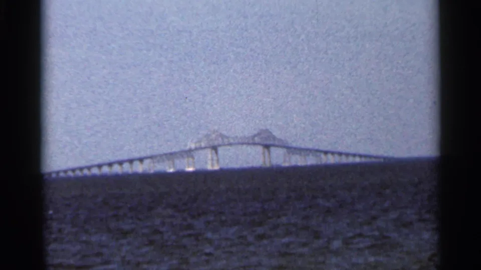 Distant Florida bridge across open water in a 1966 home-movie frame, with visible piers, soft focus, and dark frame borders.