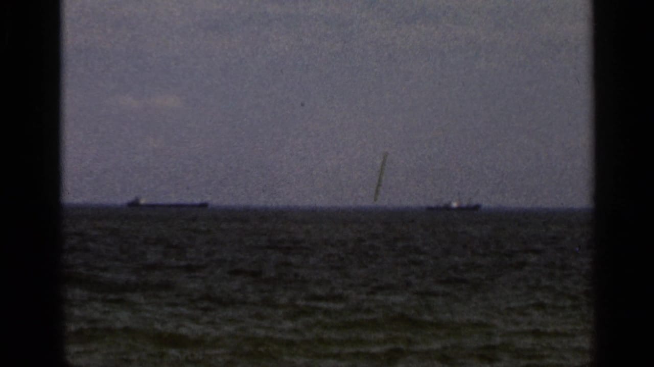 1966 Florida coastal home-movie frame showing a grey sea horizon, distant ships, and overcast sky through dark 8mm frame edges.