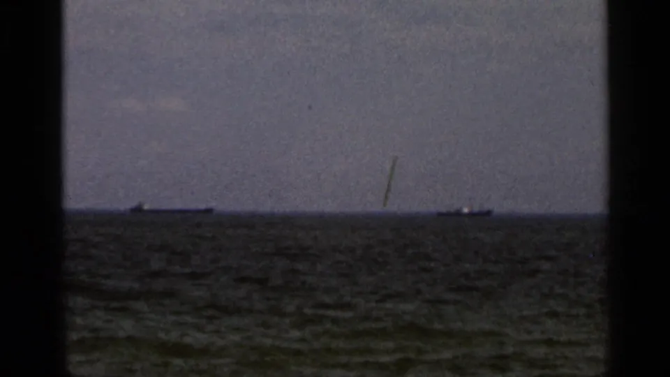 1966 Florida coastal home-movie frame showing a grey sea horizon, distant ships, and overcast sky through dark 8mm frame edges.