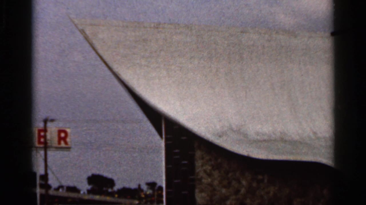 1966 Florida home-movie frame showing a partial waterfront roofline, red letters on a sign, and water beyond the structure.