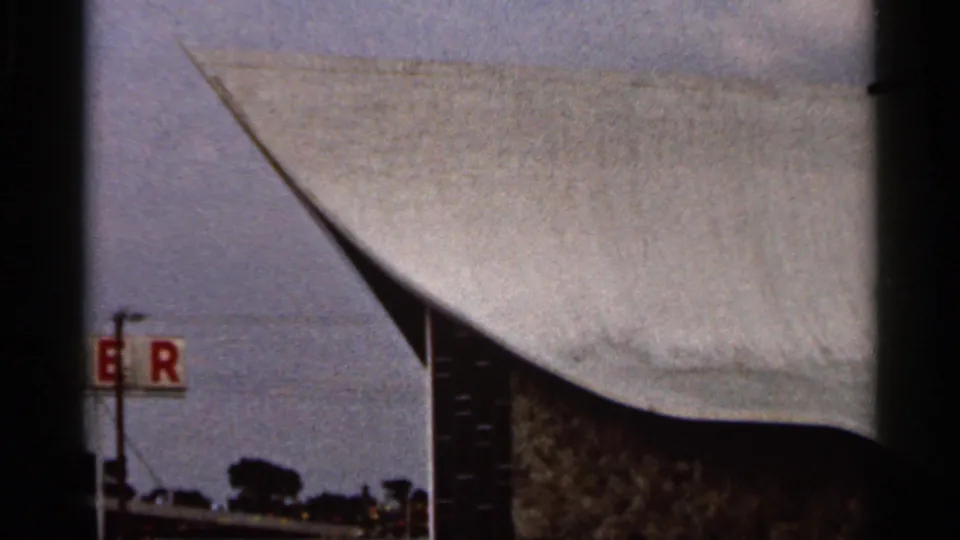 1966 Florida home-movie frame showing a partial waterfront roofline, red letters on a sign, and water beyond the structure.