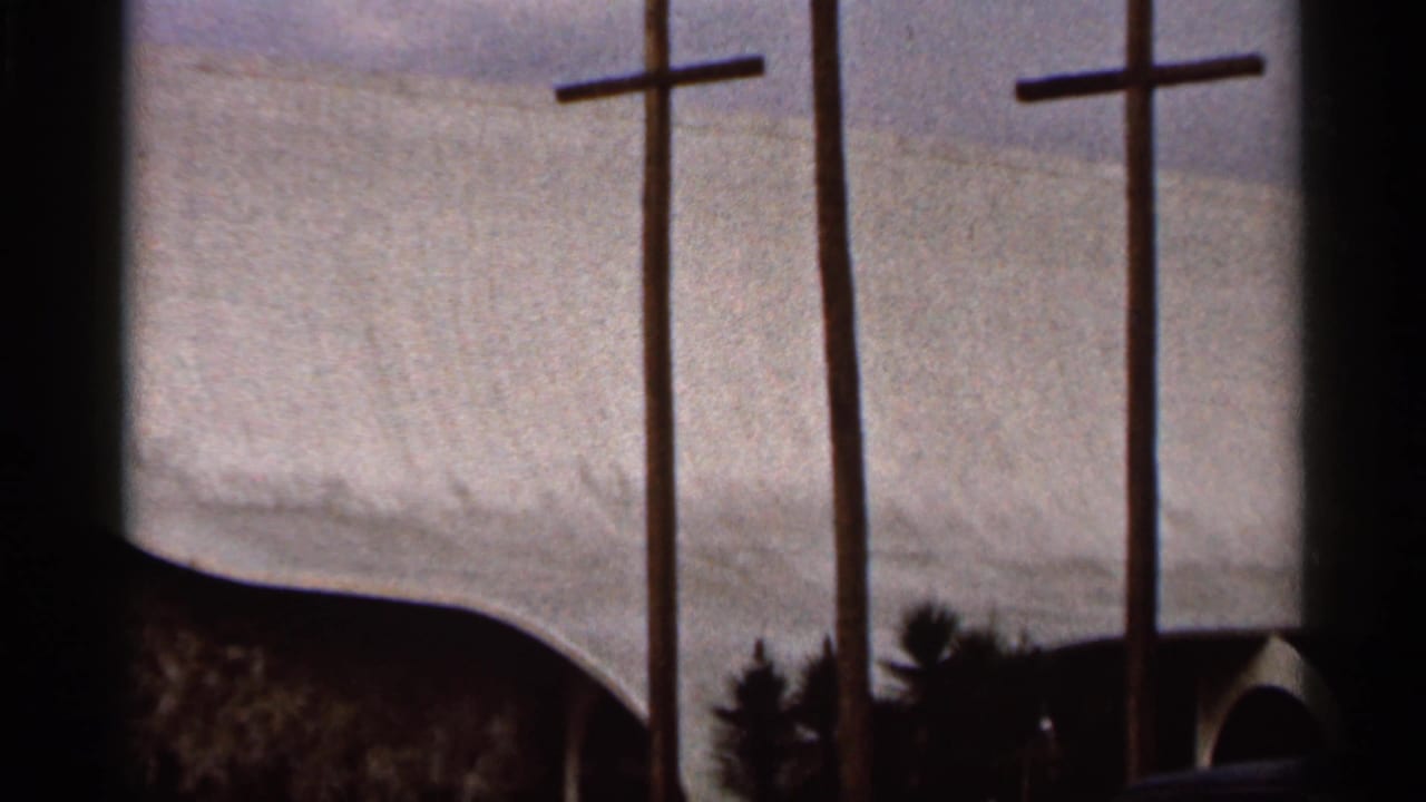 1966 Florida 8mm view of three wooden crosses in front of a modern church facade with a broad curved roof and arched bays.