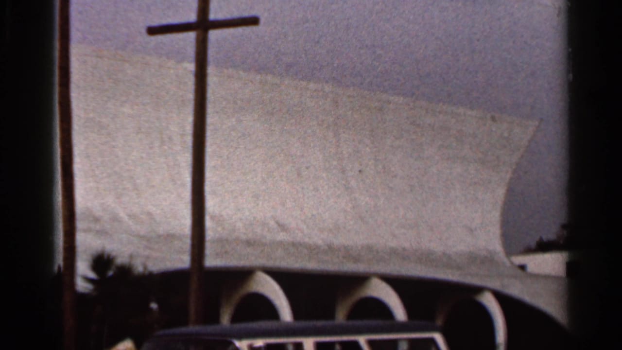 1966 Florida frame showing the modern church exterior with three crosses, arched openings, foliage, and a classic car roof at the bottom edge.
