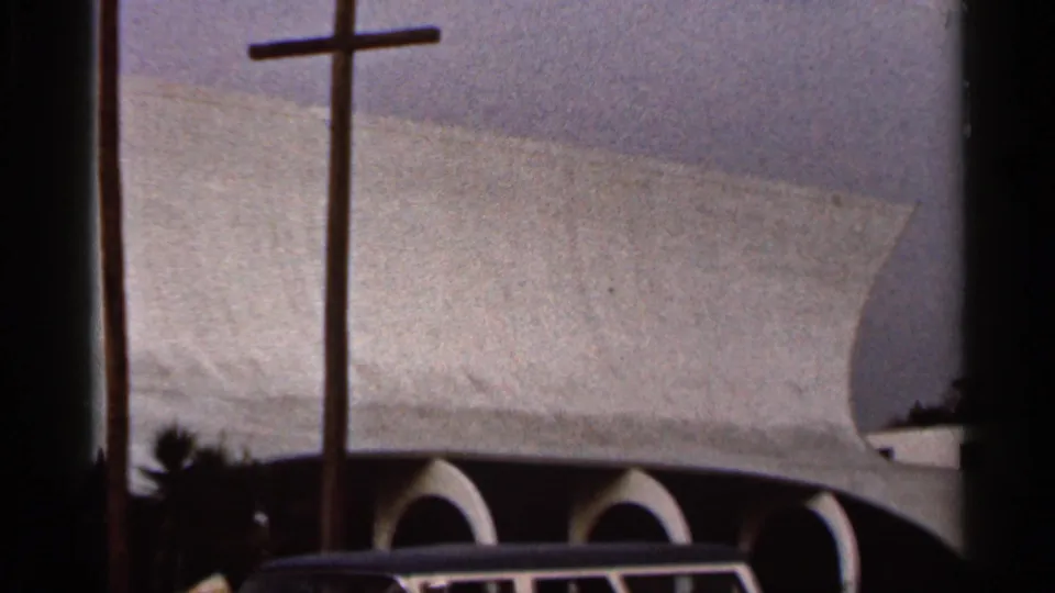1966 Florida frame showing the modern church exterior with three crosses, arched openings, foliage, and a classic car roof at the bottom edge.
