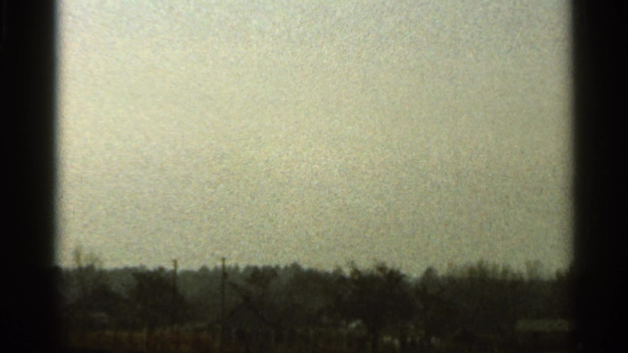 A grainy 1966 Florida 8mm frame shows a low tree line and possible distant rooftops under a muted evening sky.