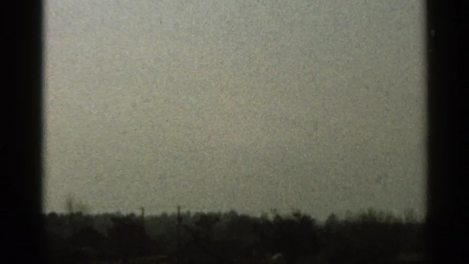 1966 Florida 8mm frame showing a pale sky, dark film borders, and a distant rural tree line beyond low brown ground.
