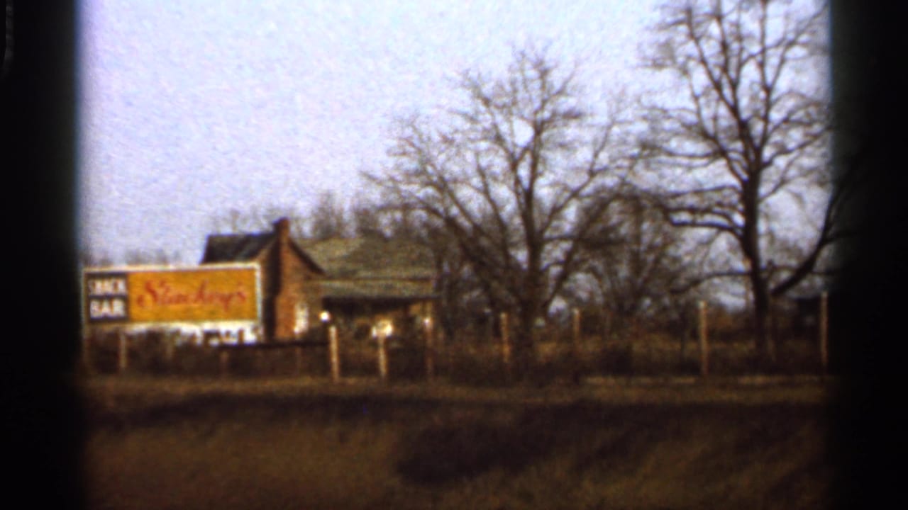 1966 Florida roadside scene with a small snack bar building, prominent yellow sign, fence line, and bare trees.