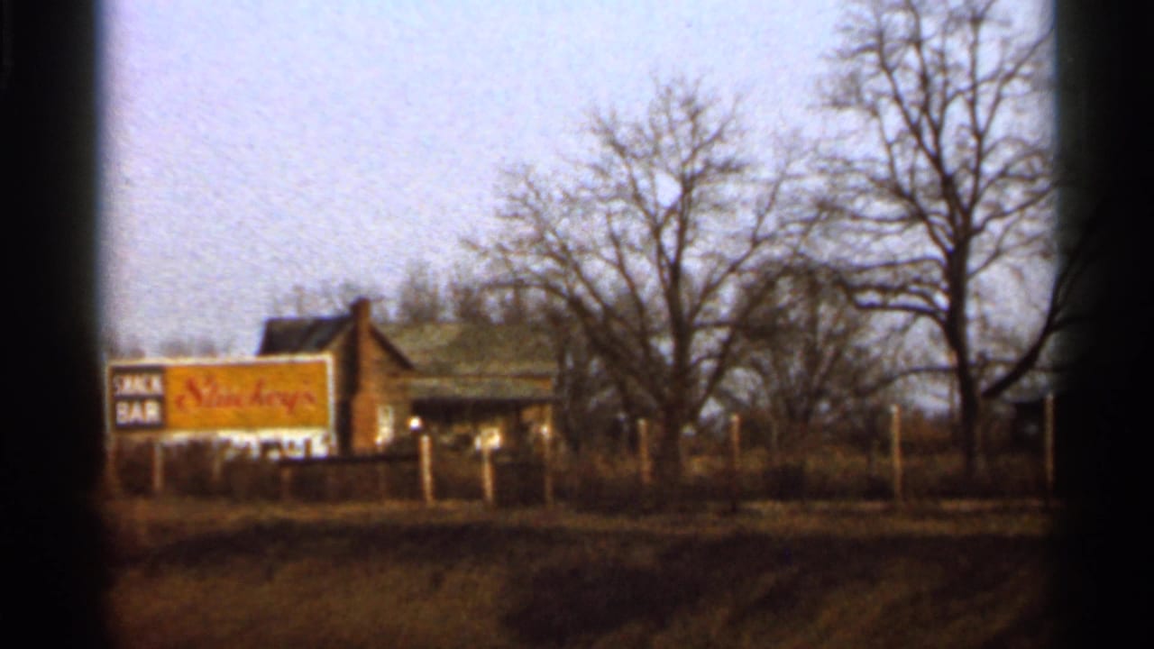 1966 Florida 8mm view of a roadside snack bar sign, low building, fence posts, and leafless trees from a passing vehicle.