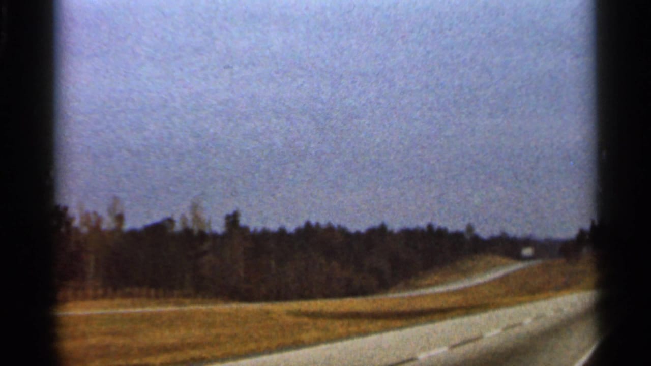 1966 Florida travel frame showing a pale winding road through open countryside with trees and a distant vehicle.