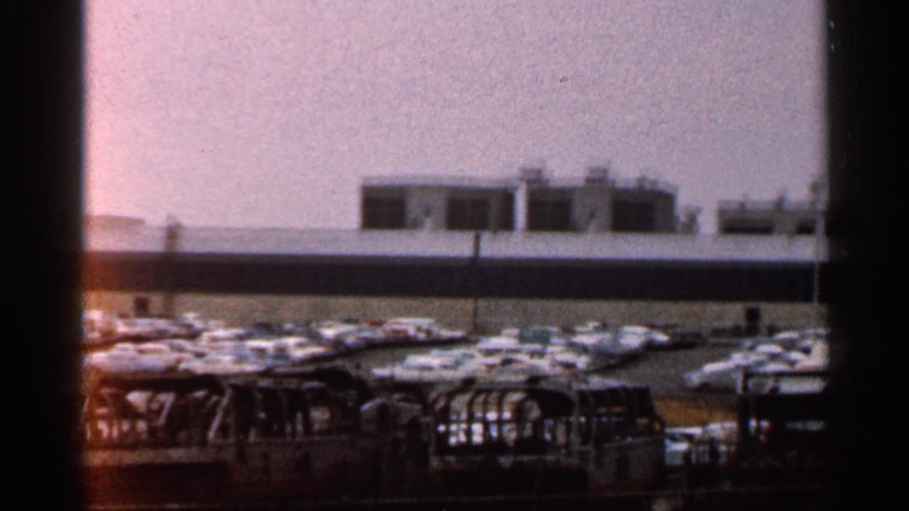 1966 Florida 8mm view of a crowded parking area beside a long low building, partially obscured by dark frame edges.