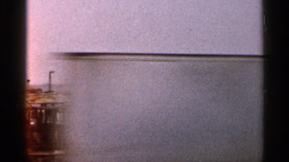 1966 Florida 8mm frame showing a low view of corrugated siding, pale sky, dark gate edges, and a partial roadside structure at left.