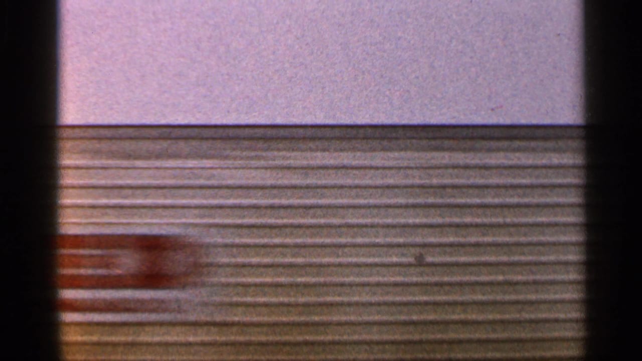 1966 Florida 8mm frame with blurred corrugated siding and a reddish moving object crossing the industrial background.