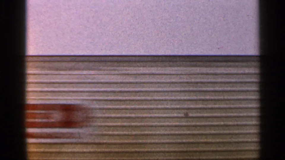 1966 Florida 8mm frame with blurred corrugated siding and a reddish moving object crossing the industrial background.