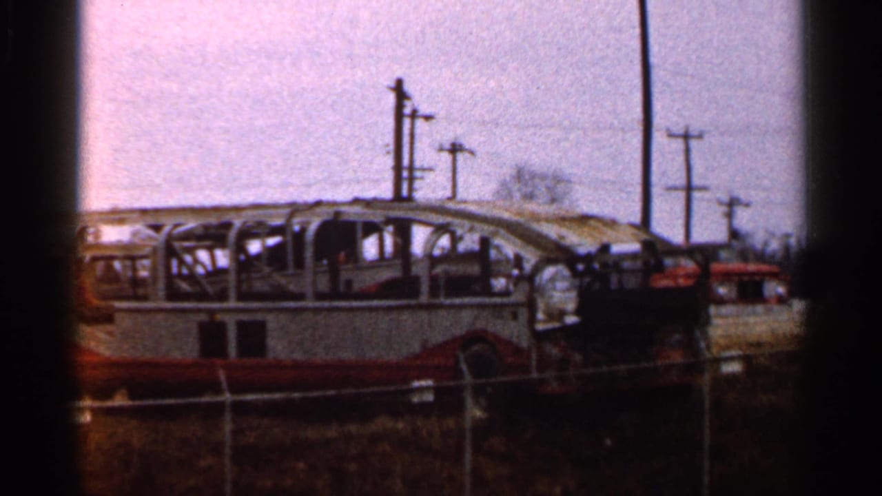 Burned bus skeleton behind a chain-link fence with utility poles in the background.