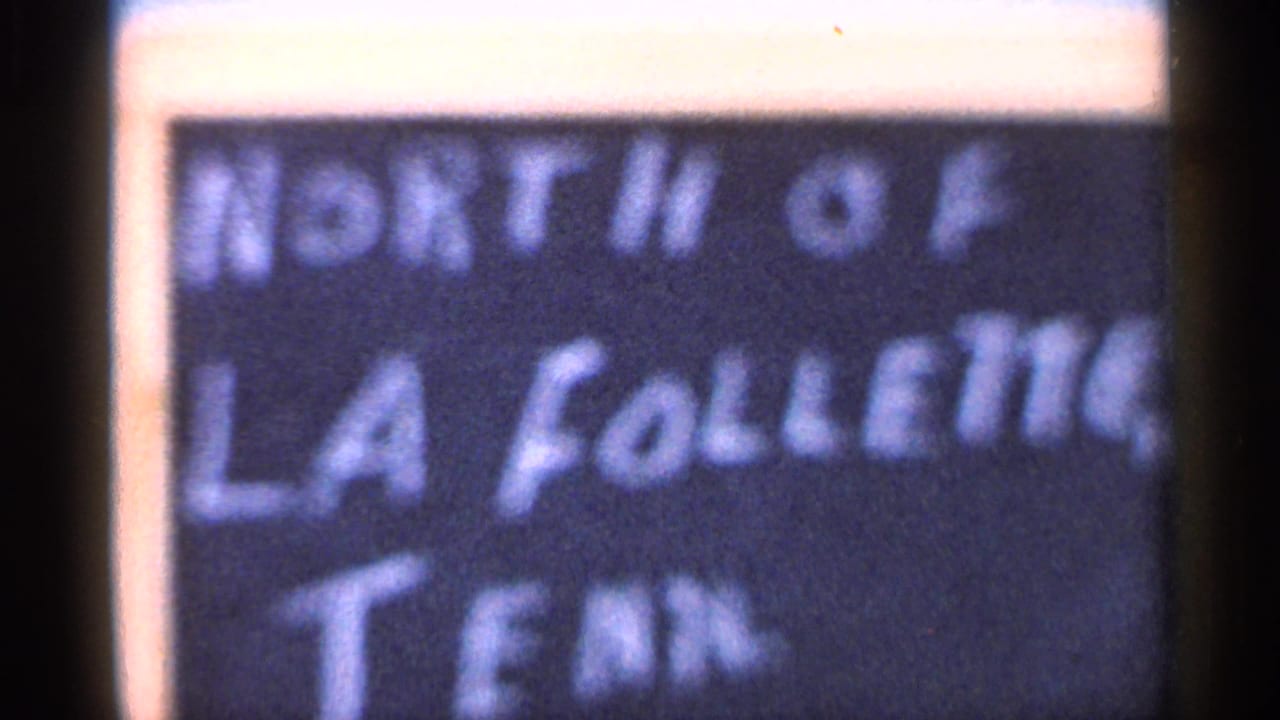 Close 8mm frame of a handwritten sign that appears to read North of La Follette, Tenn., filmed after the bus view.