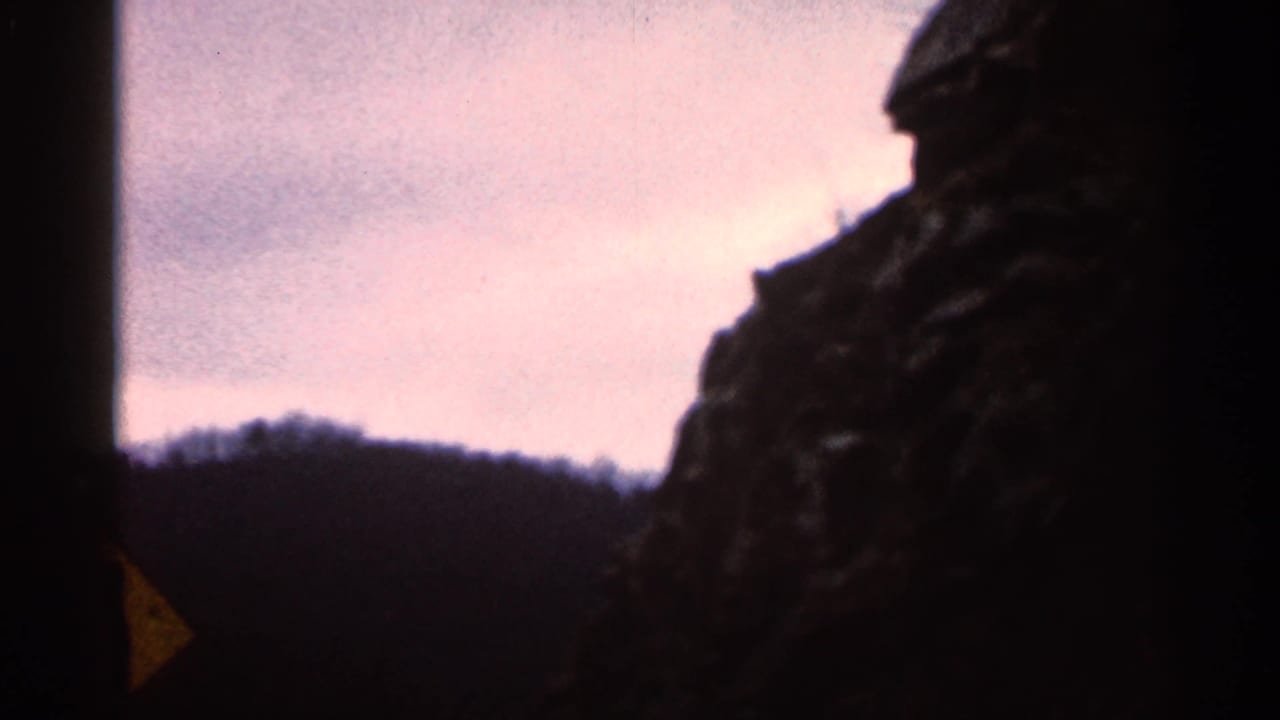 Misty mountain ridge seen from a car window with a dark rock face and partial yellow road sign.