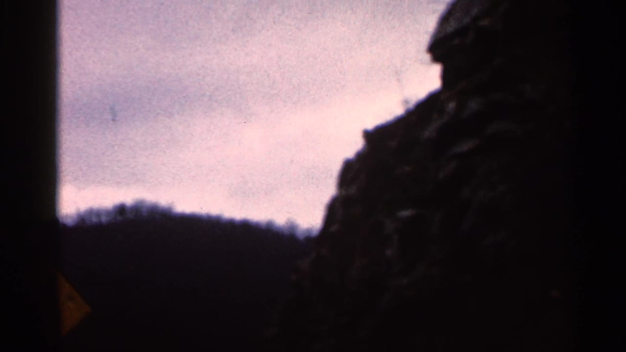 Foggy ridge and dark roadside rock framed by the vehicle interior under a pale sky.